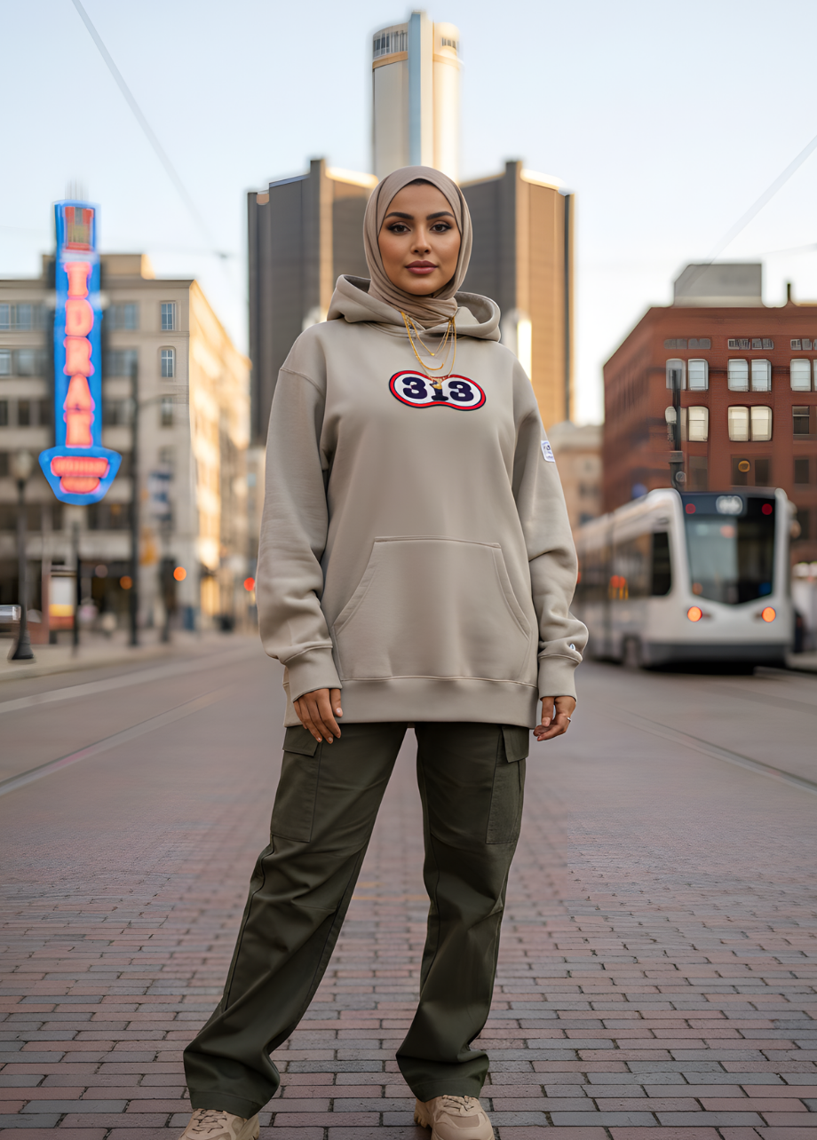 Person wearing a beige hoodie with a logo and green pants standing on a city street.