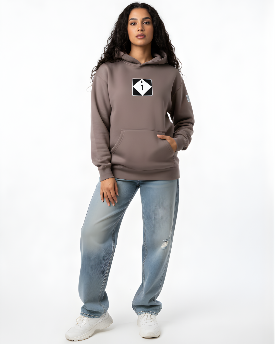 Person wearing a brown hoodie with a logo and light blue jeans on a white background