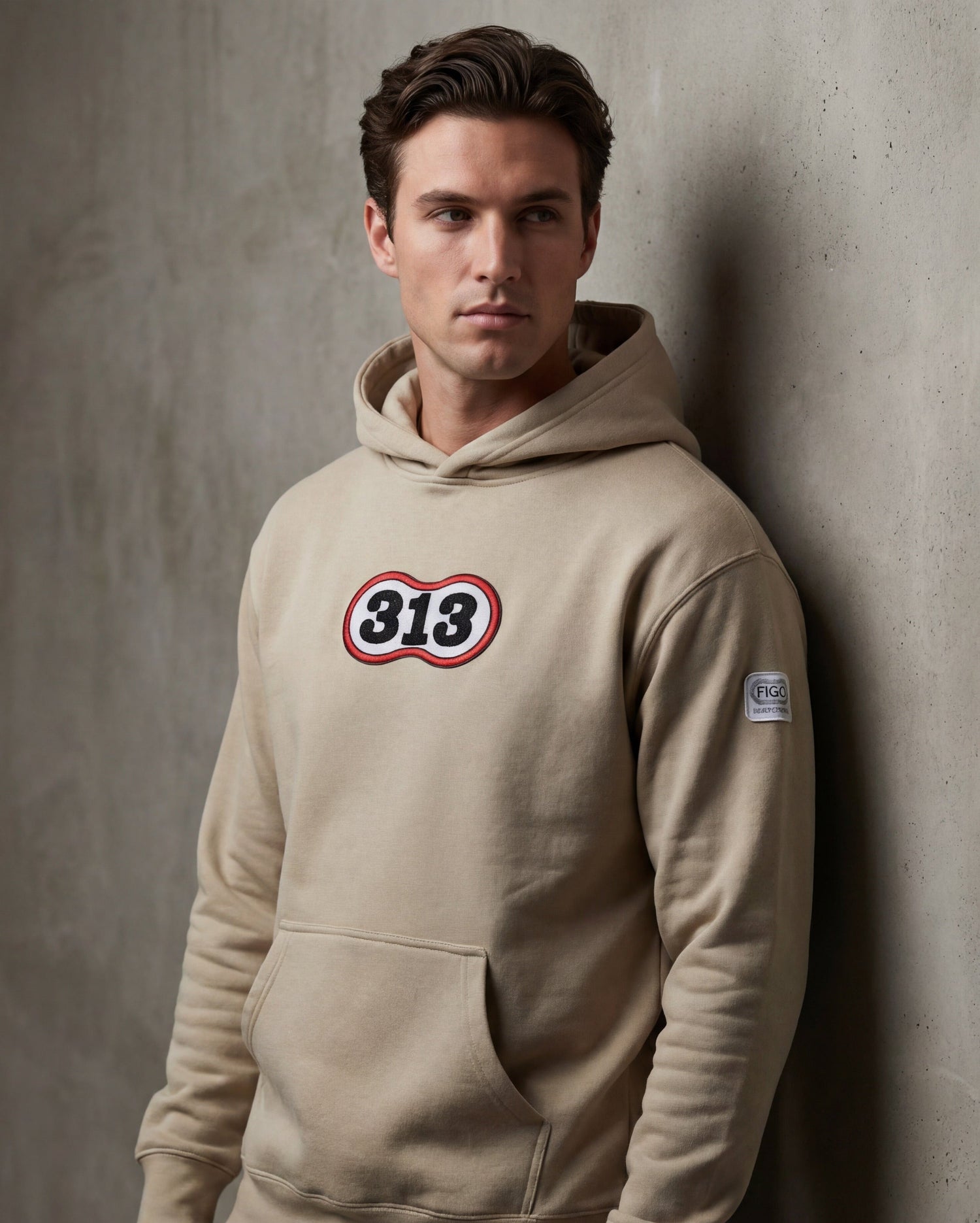 Man wearing a beige hoodie with a logo against a gray wall